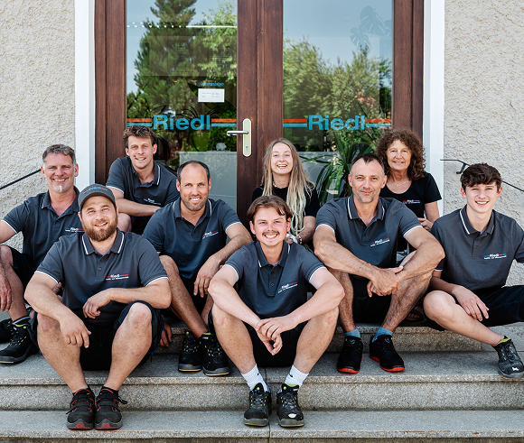 Das Team von Riedl Sanitär- und Heizungstechnik Marktoberdorf sitzt vor dem Firmengebäude des Handwerksbetriebs